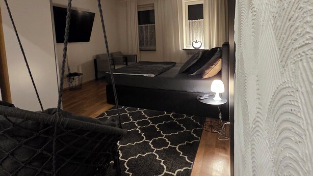 Een moderne slaapkamer met een zwevend bed, een slaapbank, een televisie en een raam met gordijnen.