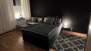 Een moderne slaapkamer met een bed, een stoel, een tafel en een raam met gordijnen.