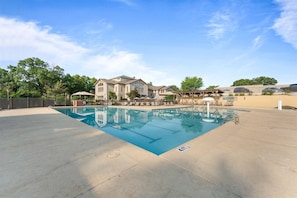A swimming pool with a clear blue water surface, surrounded by a concrete deck.
