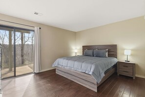A bedroom with a large bed, a nightstand with a lamp, a sliding glass door, and a view of trees. - Overlook Paradise  Scenic Stay (Branson)