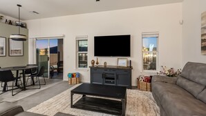 A modern living room with a flat-screen TV, a dining area with a table and chairs, and a sofa. - Sunset Pool Home Retreat Sleeps 11 Close to River (Bullhead City)