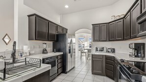 A modern kitchen with dark cabinets, white countertops, a built-in dishwasher, and a central island with a sink. - Sunset Pool Home Retreat Sleeps 11 Close to River (Bullhead City)