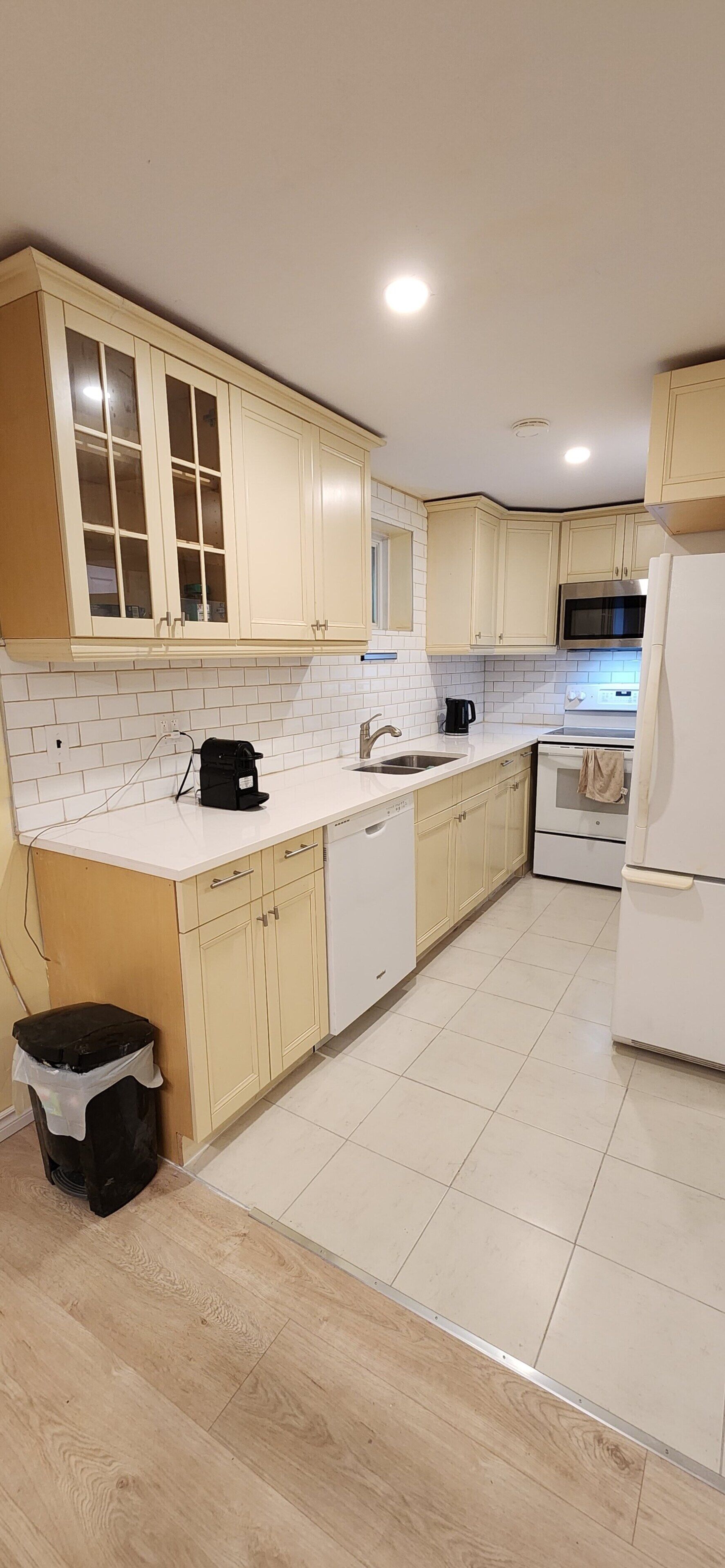 A kitchen with light-colored cabinets, a white countertop, a stainless steel microwave, and a white refrigerator.