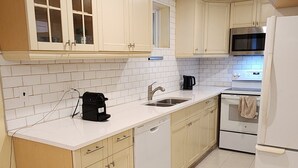 Cucina con mobili chiari, un piano di lavoro bianco, un forno a microonde in acciaio inossidabile e un frigorifero bianco.