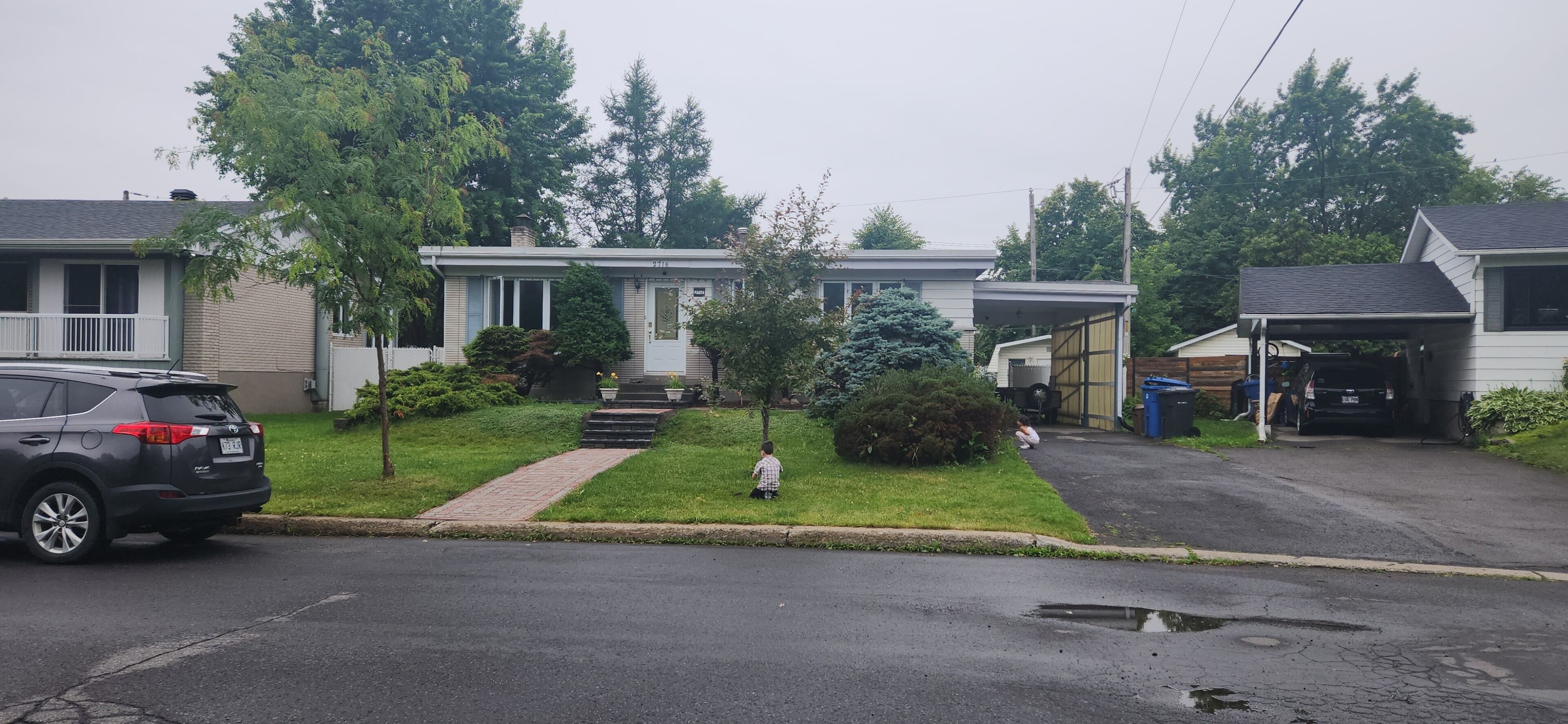 A residential street with houses, a parked SUV, and a person walking.