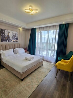 Ein Hotelzimmer mit einem großen Bett, einem Bild an der Wand, Blick durch das Fenster und einem Sessel.