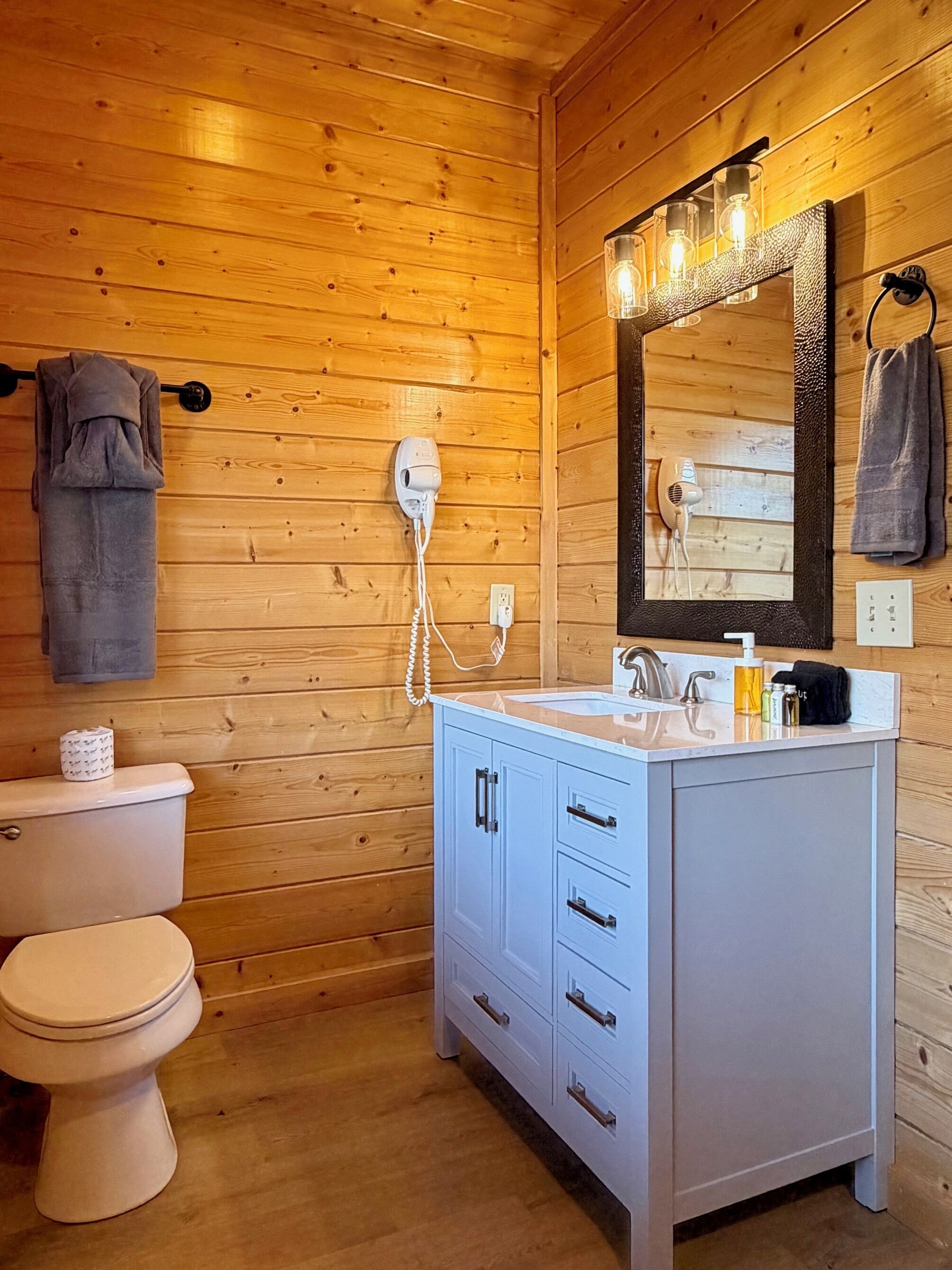 A wooden-paneled bathroom with a white toilet, a vanity with drawers, a mirror with lights, and a towel hanging on a rack.