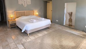 Quarto com cama, luminárias de cabeceira, um pendente de macramé, um tapete tecido e uma porta.