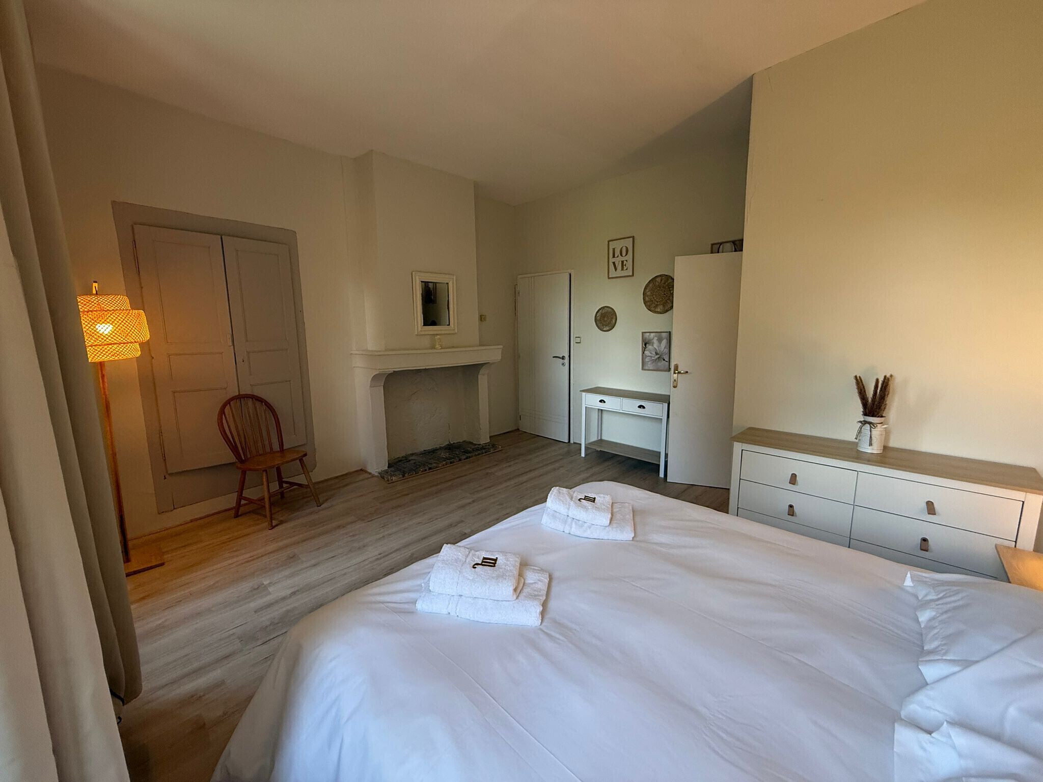 Ett hotellrum med en säng, ett skrivbord, en stol, en garderob och en öppen spis.