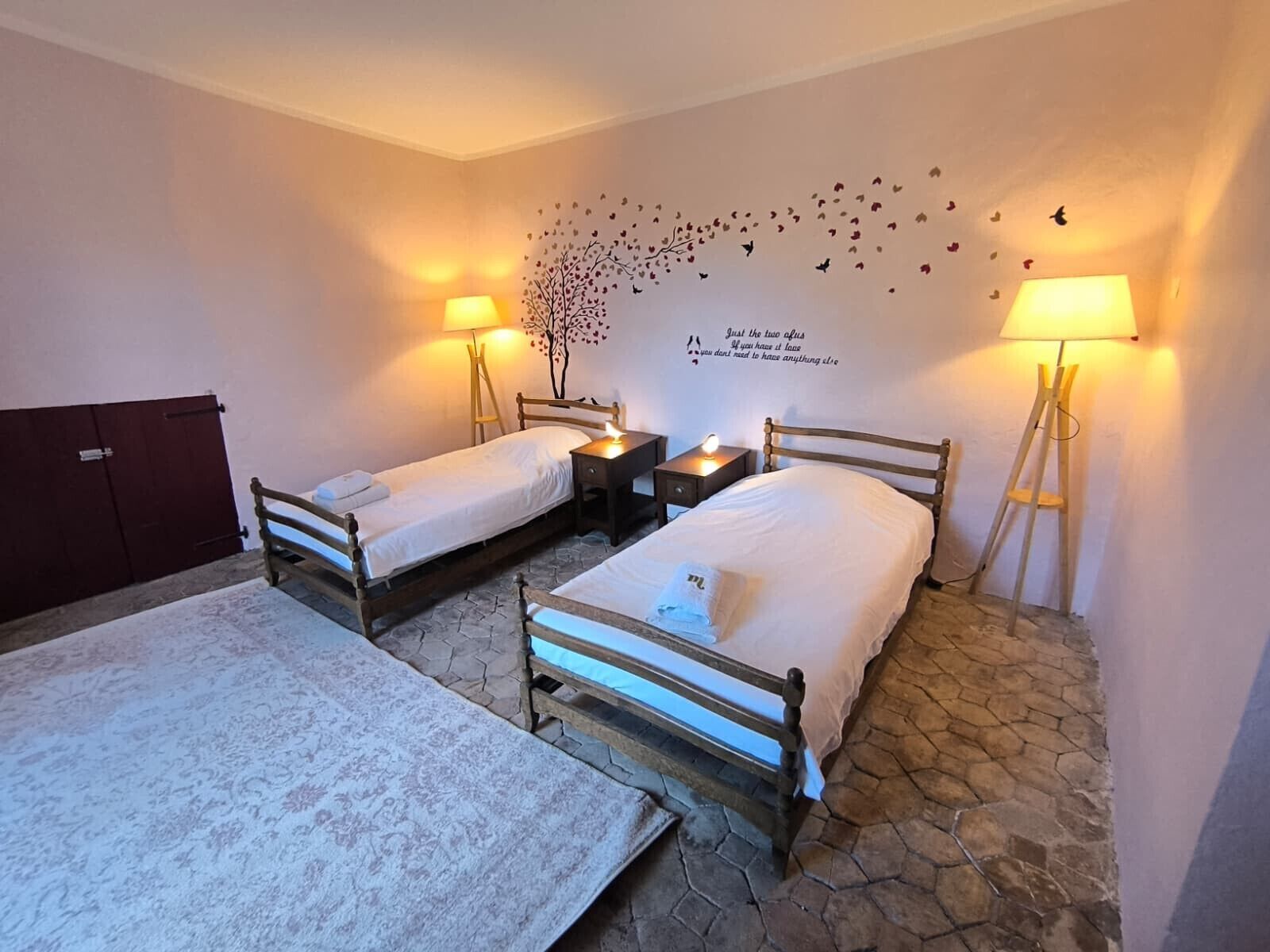 Ein Zimmer mit zwei Einzelbetten, einem kleinen Tisch, zwei Nachttischlampen, einer Wanddekoration und einem roten Schrank.