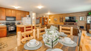 Een keuken met houten kastjes, een magnetron en een koelkast. Er is een eethoek met een houten tafel voor vier personen, omringd door houten stoelen.