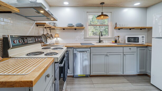 A modern kitchen with a stove, microwave, and dishwasher, wooden countertops, and a window with a view. - Deck & Spacious Yard! Wilmington Gem on Half-Acre (Wilmington)