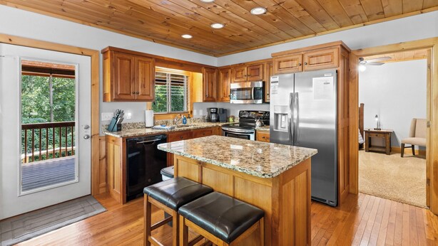 Una cocina con armarios de madera, encimeras de granito, un refrigerador de acero inoxidable y techo de madera.