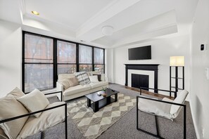 A modern living room with a sofa, coffee table, fireplace, and large windows.