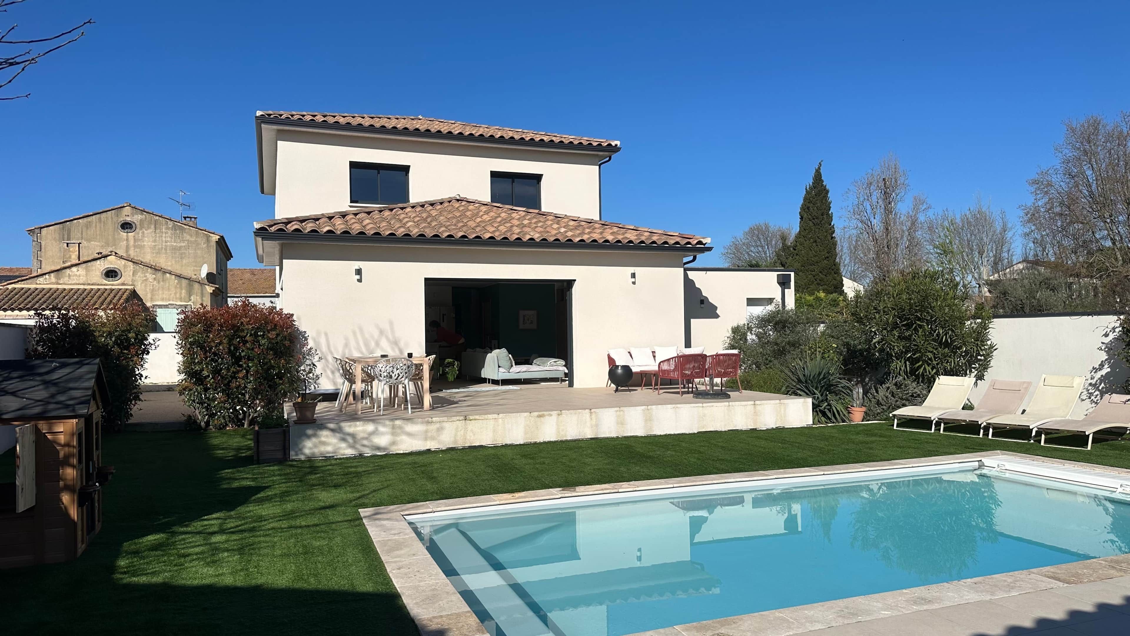 Une maison moderne à deux étages, dotée d’une piscine, d’un patio avec mobilier d’extérieur et d’une pelouse bien entretenue.
