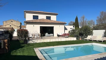 Une maison moderne à deux étages, dotée d’une piscine, d’un patio avec mobilier d’extérieur et d’une pelouse bien entretenue.