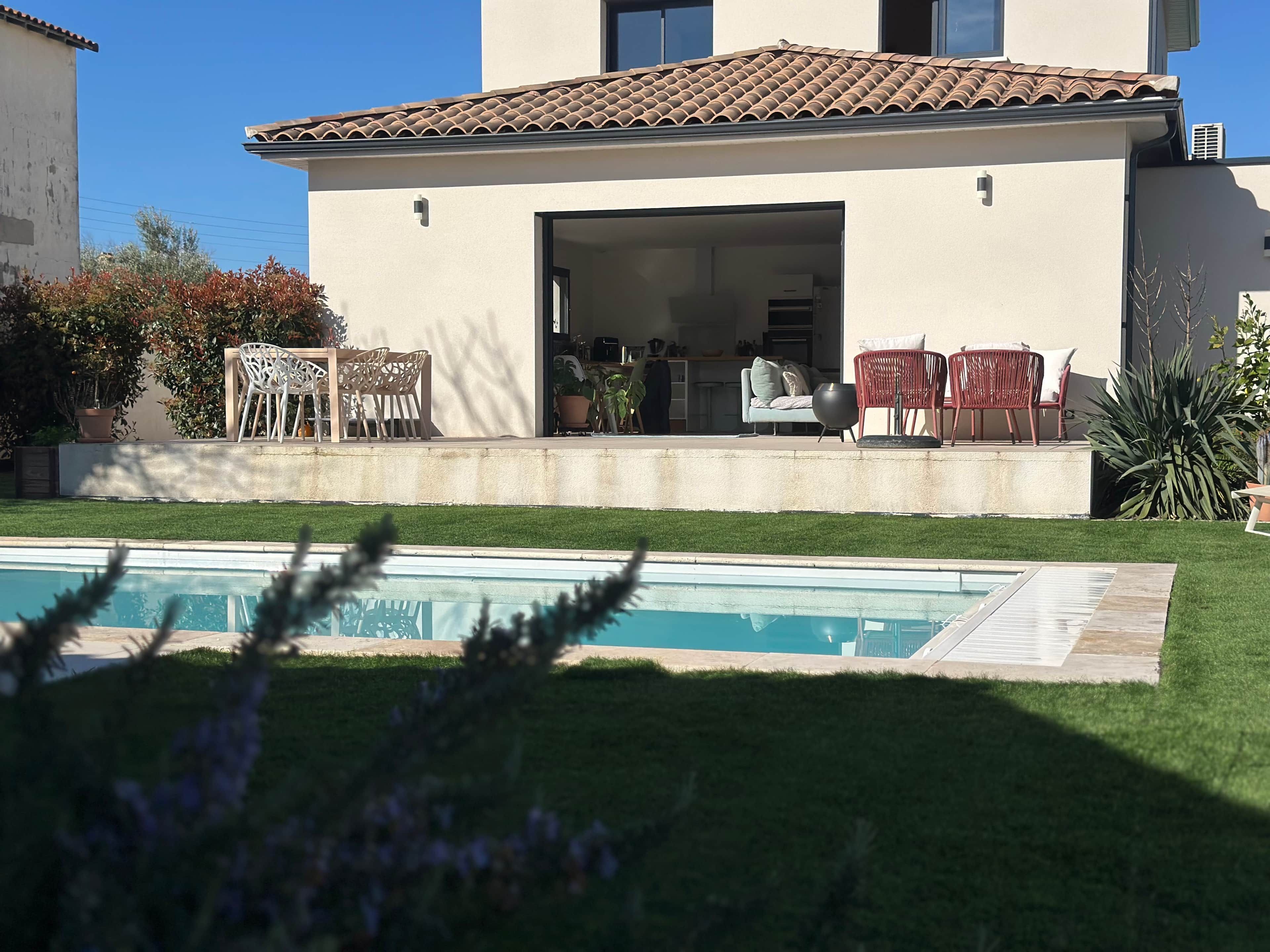 A modern house with a pool, outdoor seating, and a well-maintained lawn.