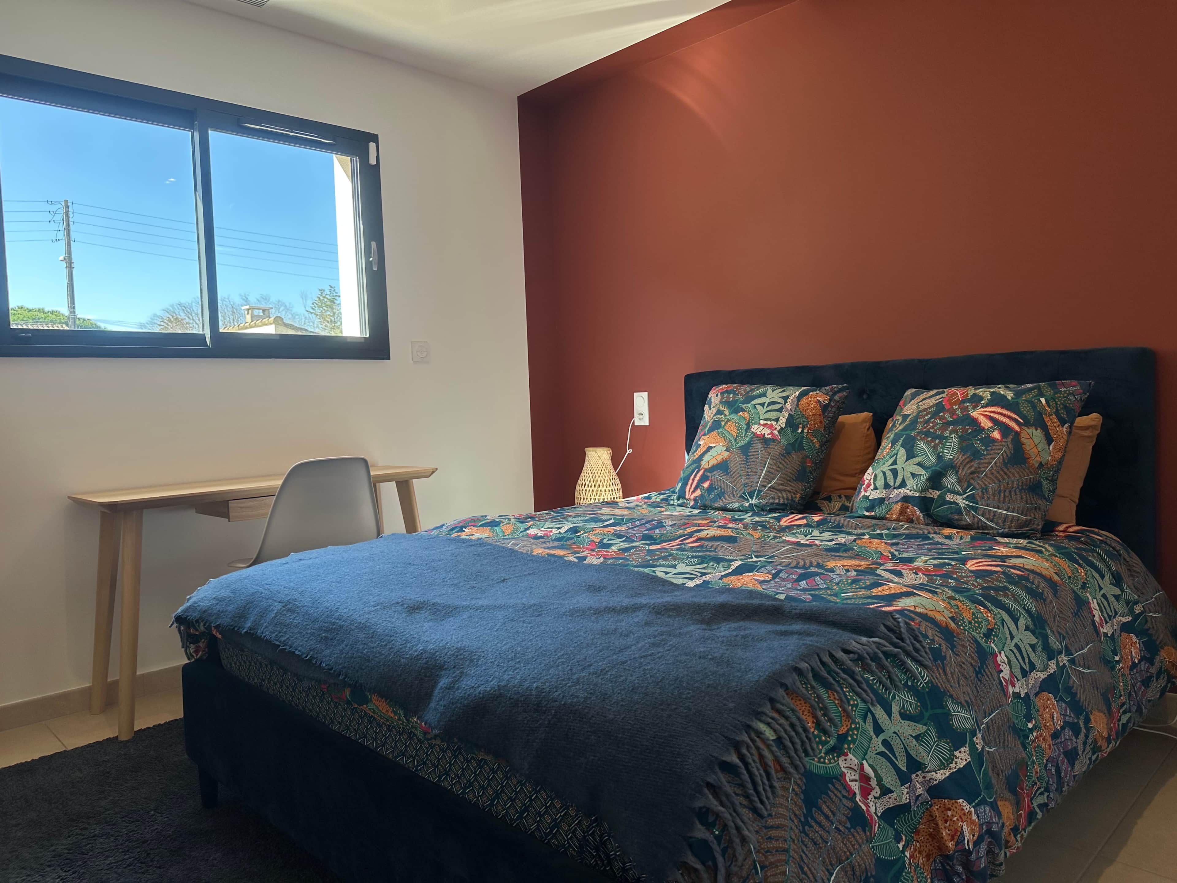 Un dormitorio con cama, escritorio y ventana.