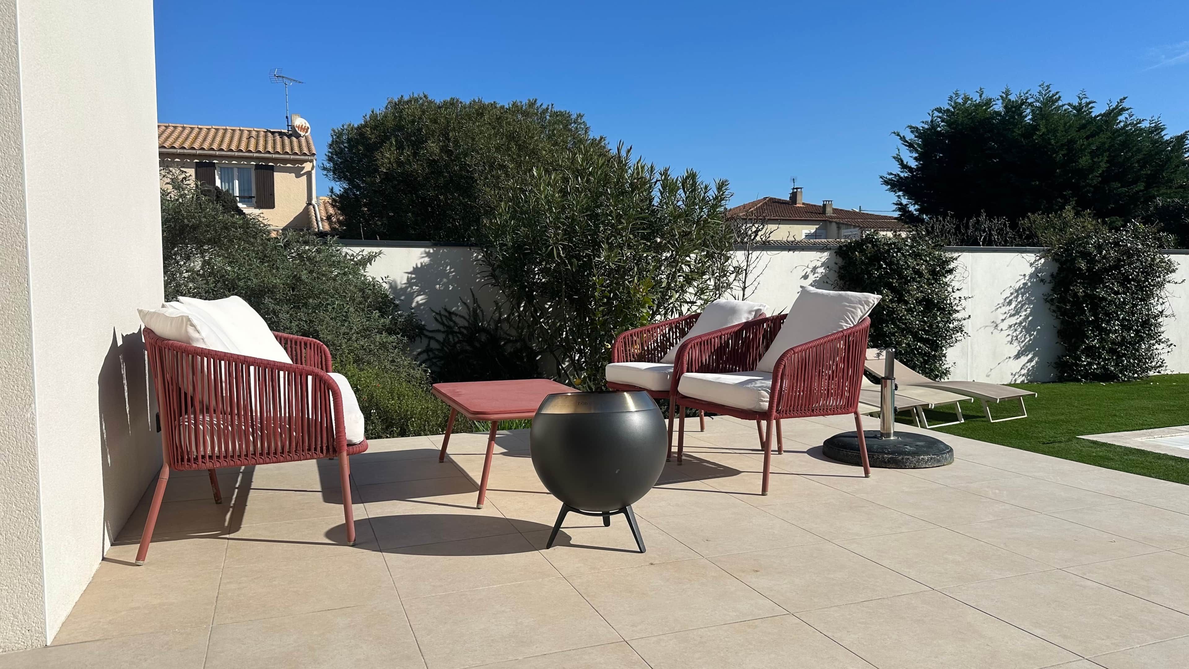 Une terrasse extérieure avec des chaises en osier, une table et un grand pot décoratif.