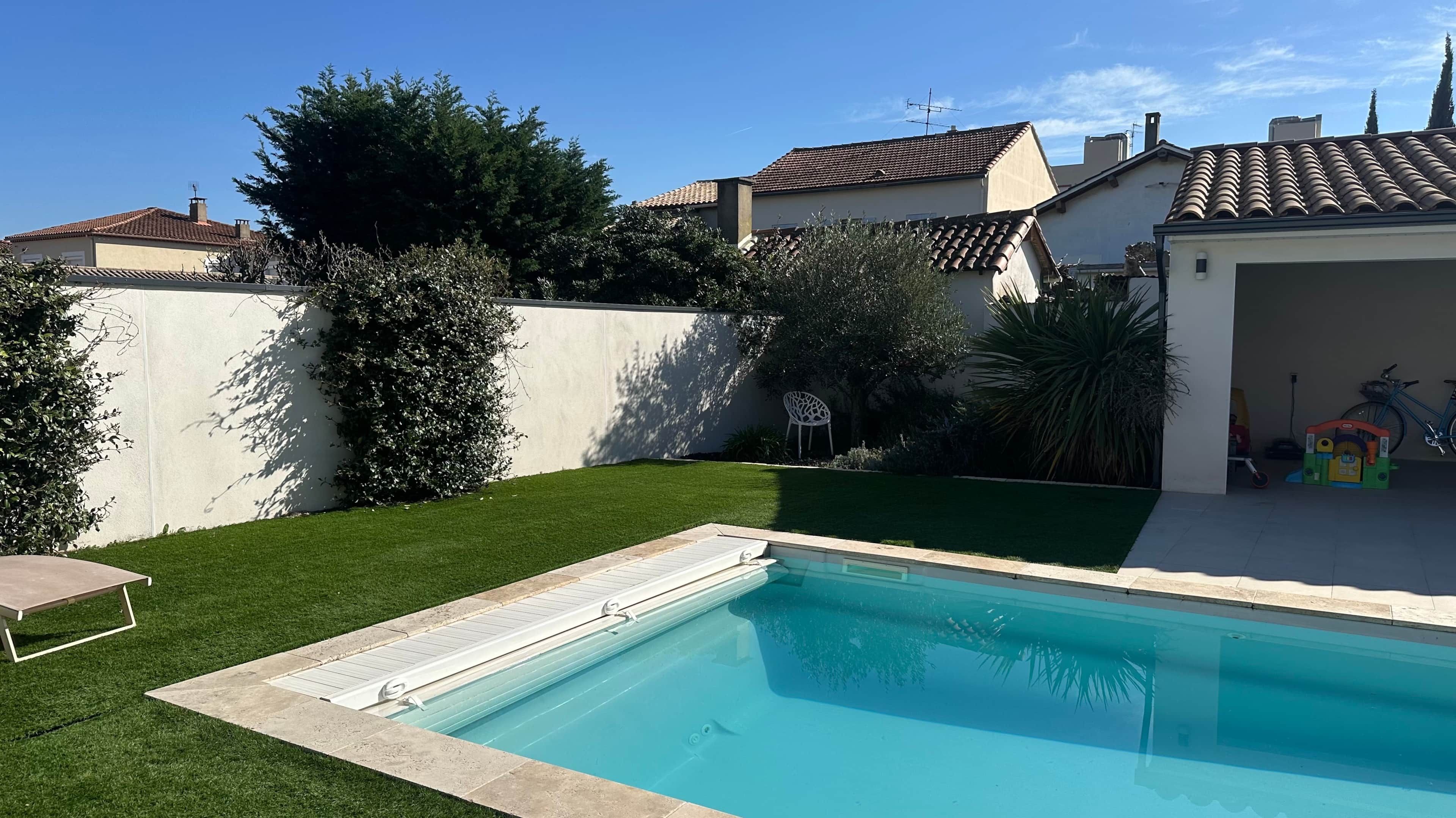 Um quintal com piscina, mesa de pátio e área coberta com uma bicicleta.