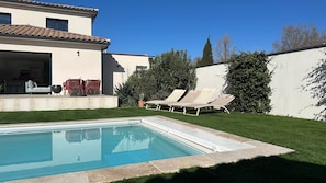 Una piscina con sillones de descanso, un patio con asientos y un césped bien cuidado.