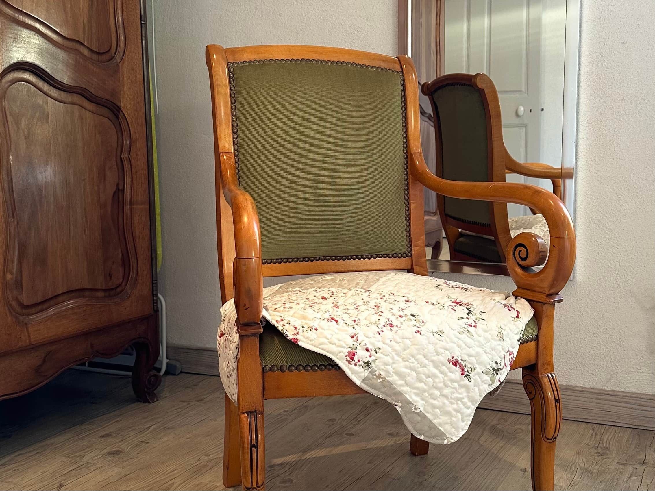 Une chaise en bois avec un dossier rembourré de couleur verte et un coussin à motifs floraux.