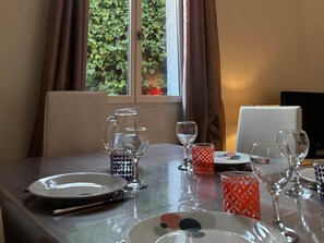 A dining table set with plates, glasses, and a pitcher, with a window view of greenery. - Le clos la Major - view of the Arles Arena (Arles)