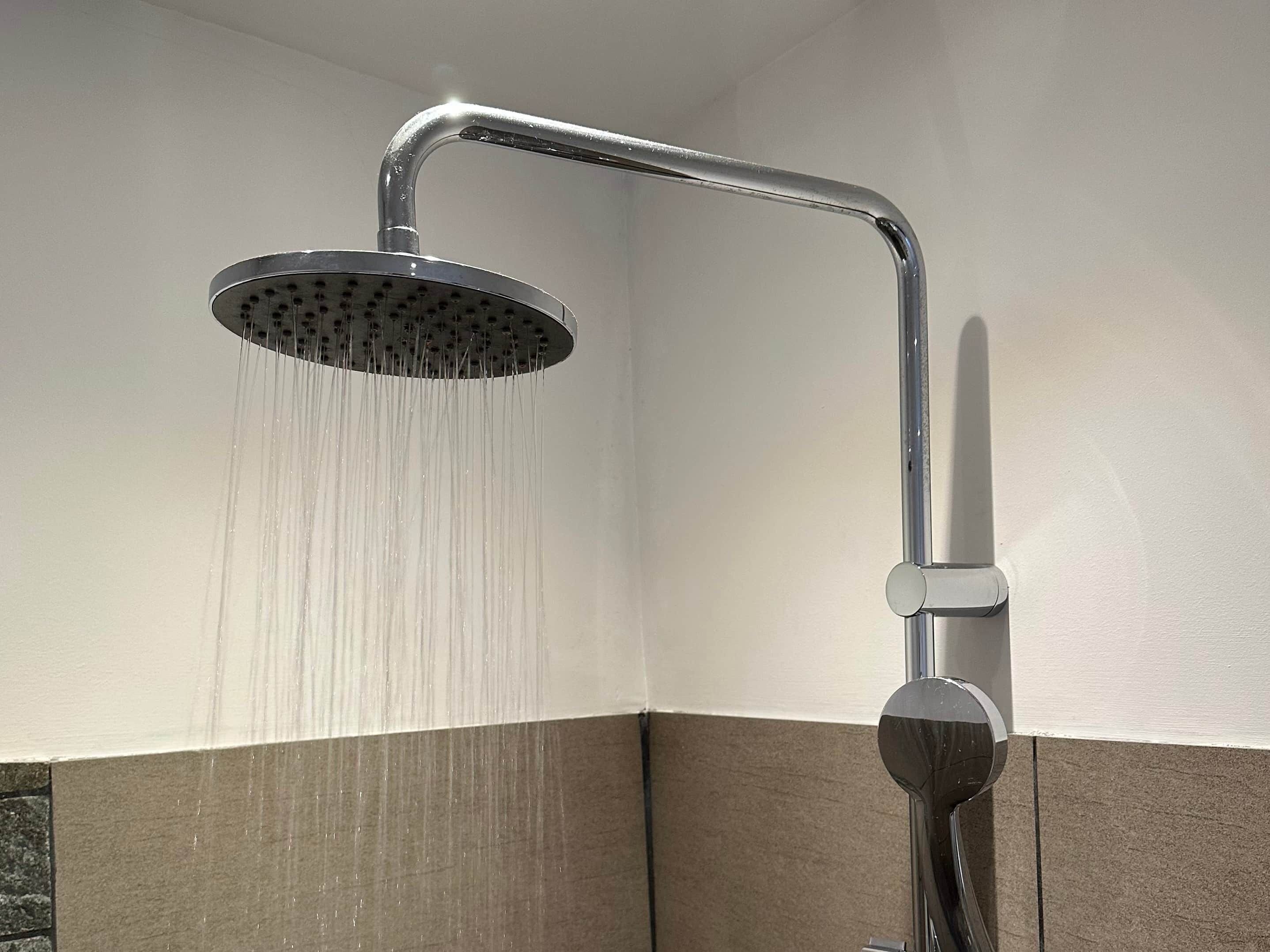 A showerhead with water running, a corner wall with a tile border, and a metal fixture.