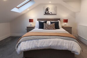 Un dormitorio con tragaluces, una cama con múltiples almohadas, lámparas de noche y una cita motivadora en la pared.