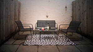 Une terrasse extérieure avec une table et quatre chaises, un tapis à motifs et une bougie.