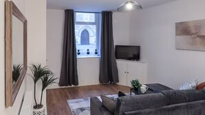 Un salon moderne avec un canapé, un téléviseur posé sur un meuble et une grande fenêtre avec des rideaux.