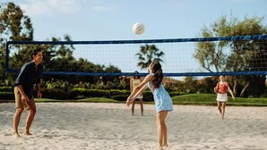 Partita di beach volley con rete, sabbia e palme sullo sfondo.