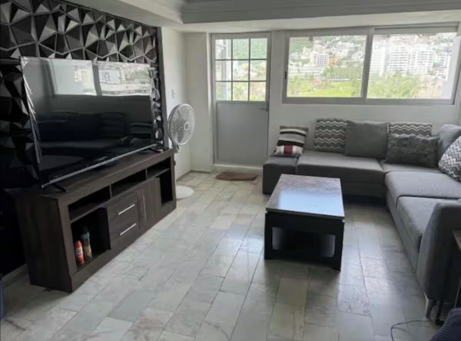 A living room with a TV, sofa, coffee table, and a window with a view of buildings.