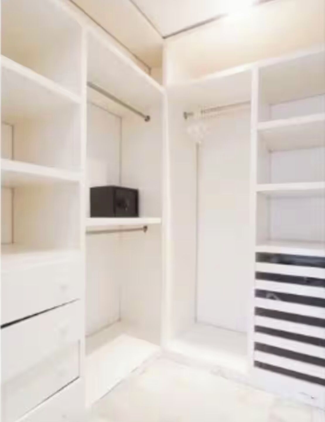 A walk-in closet with multiple shelves and drawers, a hanging rod, and a black object on a shelf.