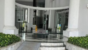 Un hall d’entrée avec un sol en marbre, des portes en verre et des colonnes blanches.