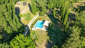 Vista aérea de una propiedad con piscina, rodeada de vegetación exuberante y un sendero despejado que lleva a la piscina.