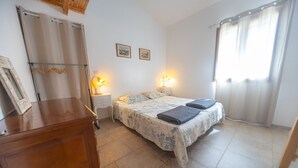 Un dormitorio con cama, lámparas de noche, un aparador de madera y una ventana con cortinas.