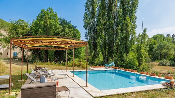 Una piscina con cubierta de madera, sillas de descanso y una pérgola.