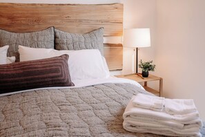 Ein ordentlich bezogenes Bett mit einem hölzernen Kopfteil, einer Nachttischlampe und einem kleinen Topfpflanzen.