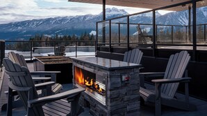 Ένα ξύλινο κατάστρωμα με καρέκλες Adirondack, μια πέτρινη εστία και ένα γυάλινο περίβλημα με τζάκι.