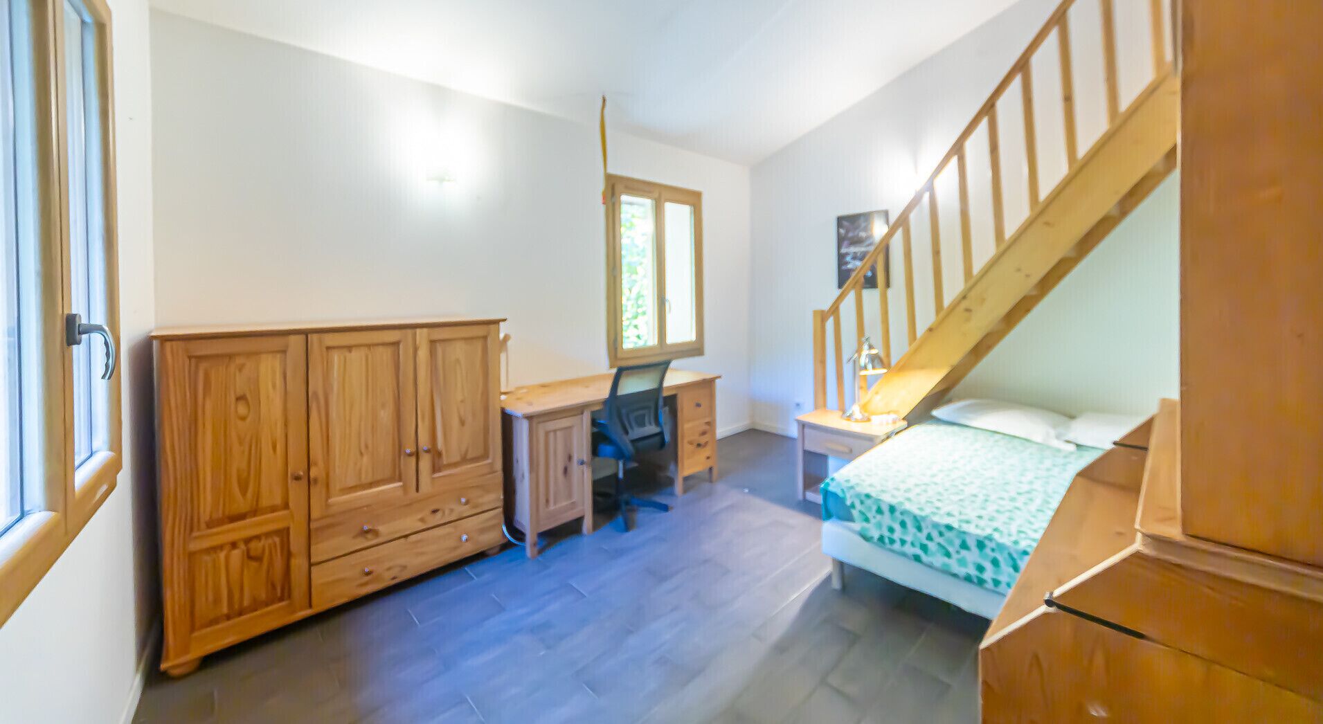A bedroom with a wooden wardrobe, a desk, a bed, and a staircase.