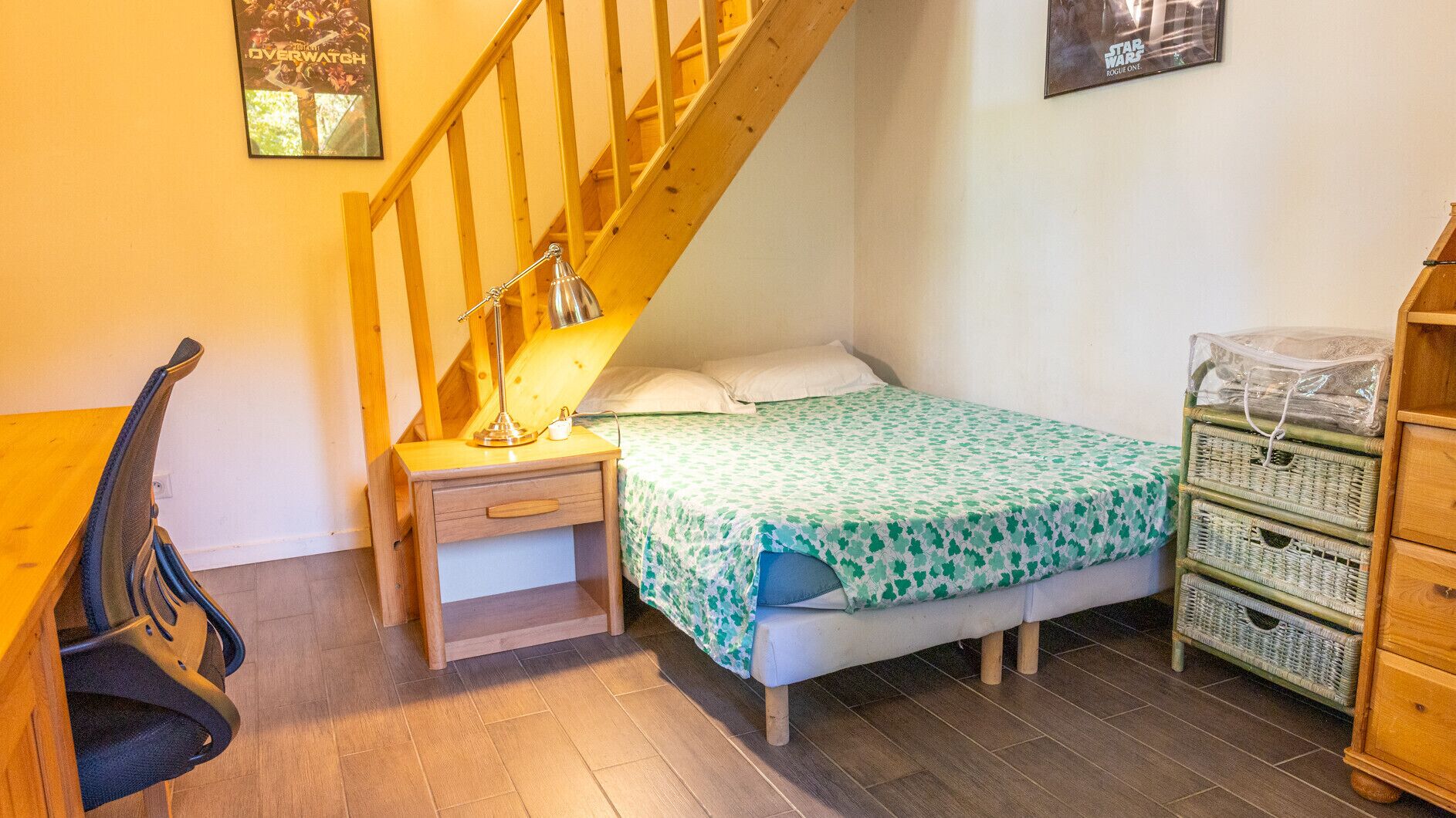 Un dormitorio con cama, mesita de noche, lámpara, silla y una escalera.