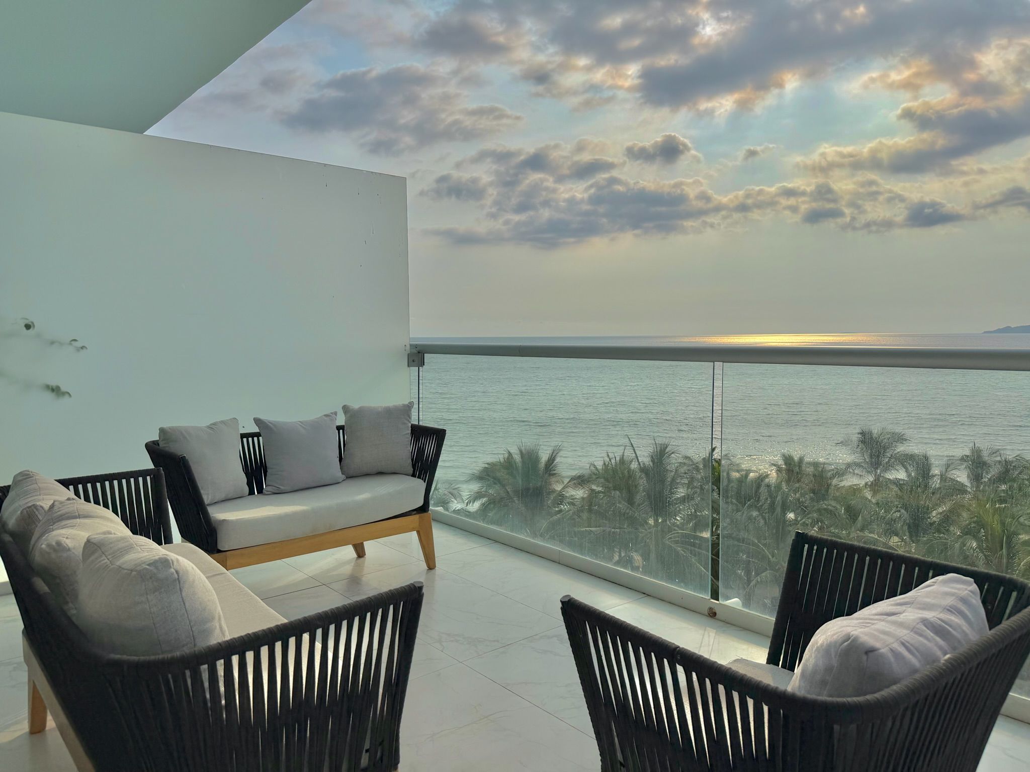 Un balcon avec un canapé et des fauteuils donnant sur une étendue d’eau.