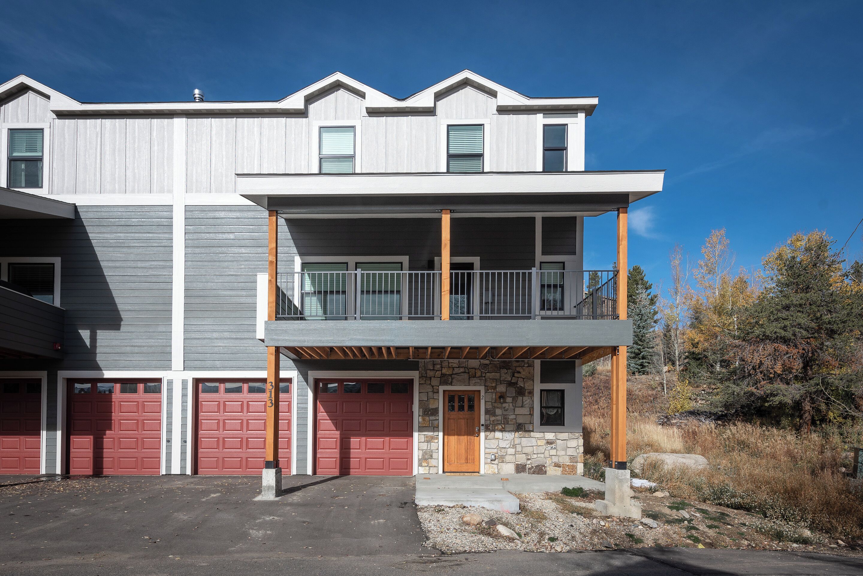 Un immeuble de deux étages doté d’un balcon, d’une façade en pierre et de portes de garage rouges.