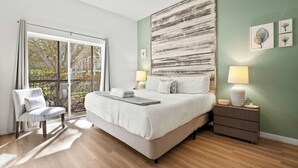 A bedroom with a large bed, a chair, a nightstand, and a view of the outdoors. - Lucaya Luxe At Bahama Bay (Davenport)