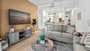 A living room with a flat-screen TV, grey sofa, and a coffee table with a plant. - Lucaya Luxe At Bahama Bay (Davenport)