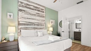 A bedroom with a large bed, bedside lamps, a nightstand, a wall art piece, and a door leading to a bathroom. - Lucaya Luxe At Bahama Bay (Davenport)