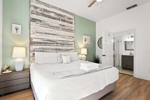 A bedroom with a large bed, bedside lamps, a nightstand, a wall art piece, and a door leading to a bathroom. - Lucaya Luxe At Bahama Bay (Davenport)