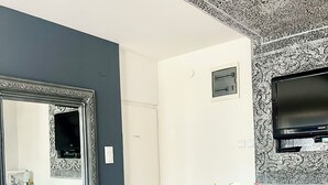 A modern room with a large mirror, a flat-screen TV, a dining table with chairs, and a vase with flowers. - Charming apartment in Pančevo with cool AC for your stay (Pančevo)