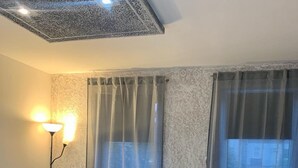 A modern living room with a sofa, a chair, a blue ottoman, a lamp, and a window with curtains. - Charming apartment in Pančevo with cool AC for your stay (Pančevo)